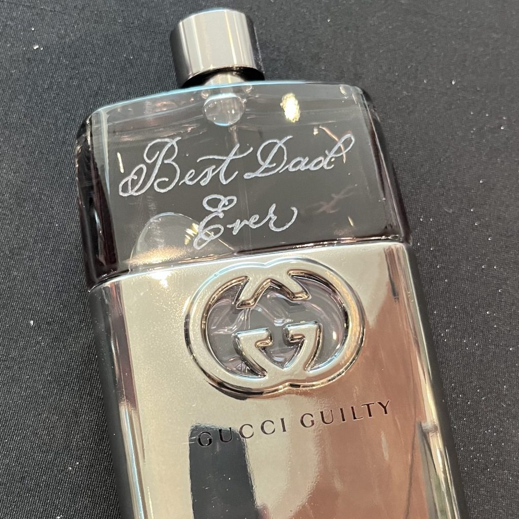 Alternate-angle view of a Burberry Hero cologne bottle engraved with “Happy Father’s Day JAC” in gold during the Gucci Father’s Day 2025 in-store event.