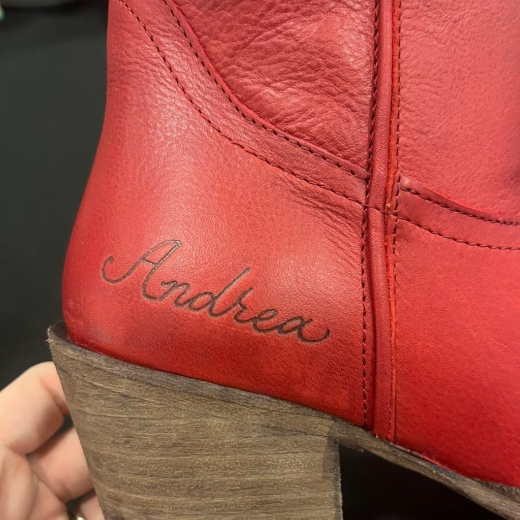 Close-up of a bright red Steve Madden boot personalized with the name “Andrea” in hand-burned calligraphy lettering on the heel, created during the Steve Madden boot-burning and hat customization bar activation at Nordstrom in the Houston Galleria by Houston calligrapher and engraver Jessica Wofford.