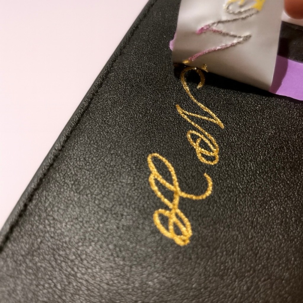 Gold foil calligraphy initials applied to a black PU leather luggage tag during a live personalization event at Nordstrom.