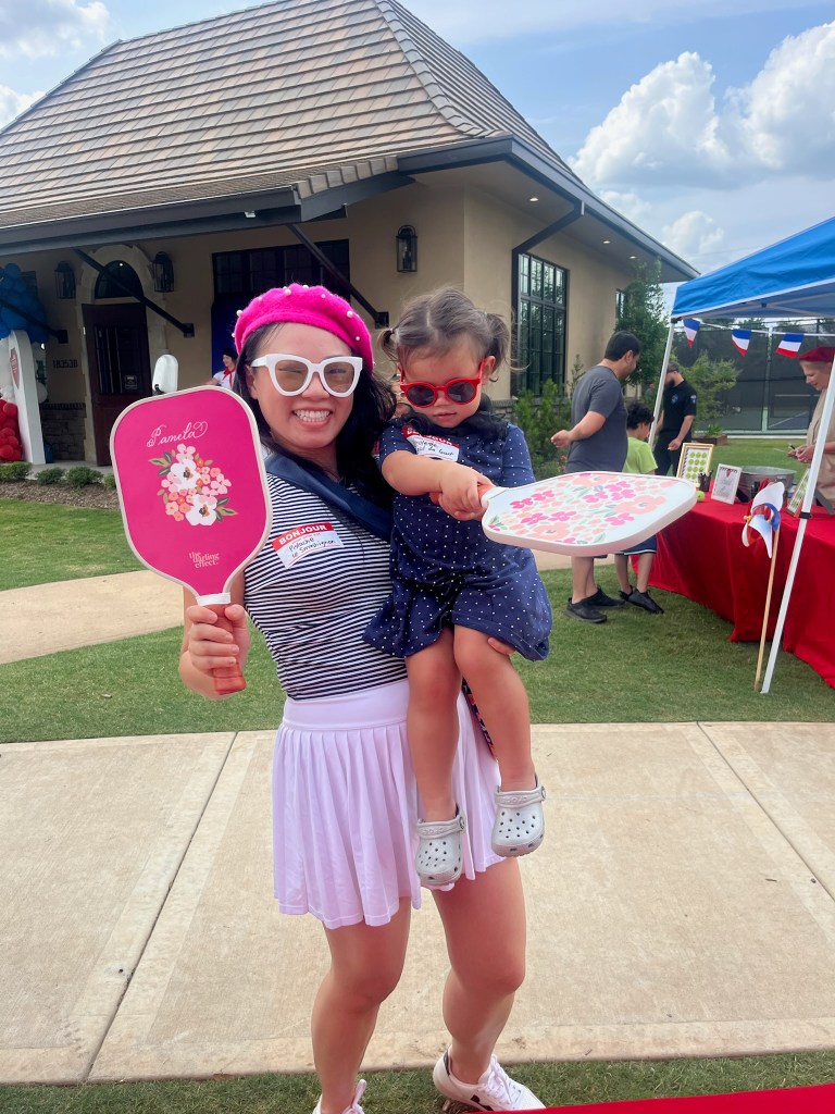 Mother and child holding personalized pickleball paddles at the grand opening of Riverstone Grand Slam Racquet Club in Texas.