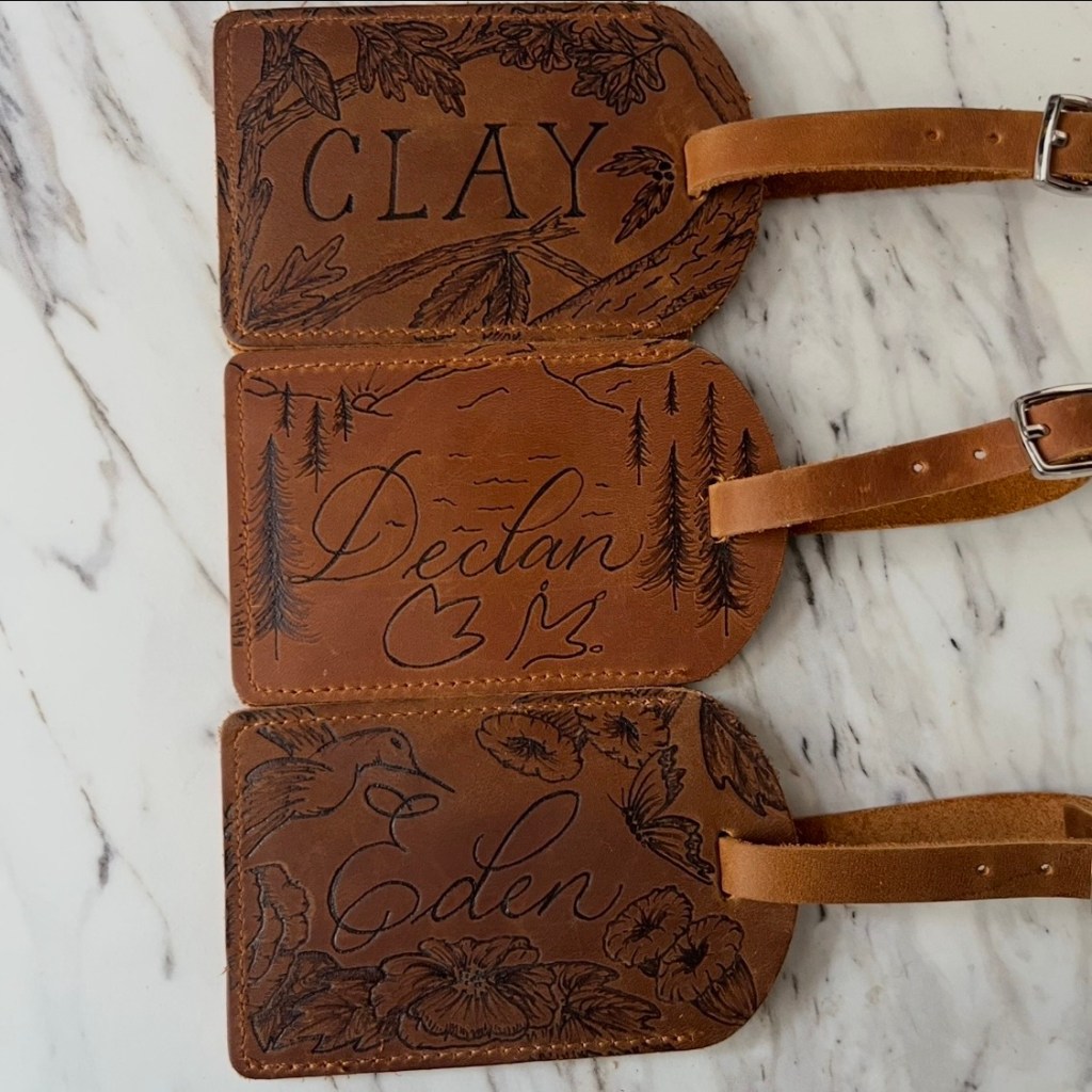 Three custom leather luggage tags hand burned with the names Clay, Declan, and Eden, created by Wofford Calligraphy. Each tag includes detailed illustrations and an NFC chip for tap to connect digital information.