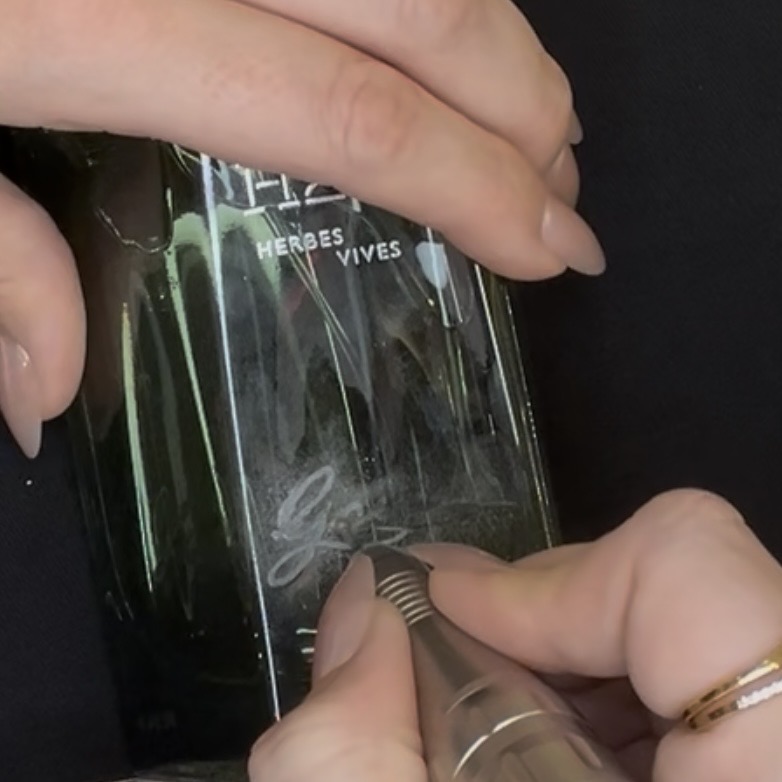 Live on-site engraving in progress on a Hermès perfume bottle during a Nordstrom Houston Galleria event, showing hand engraving and luxury personalization