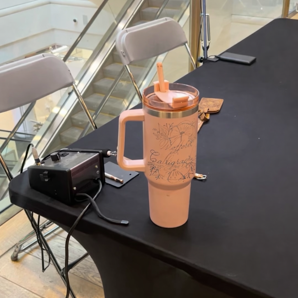 Engraved pink business cup displayed on a table at a mall with an escalator in the background, showing how branded drinkware is visible in high-traffic public spaces