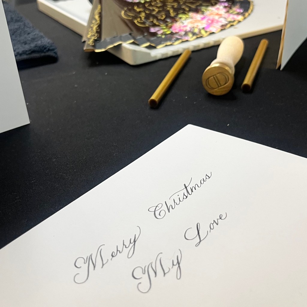 Dip pen calligraphy Christmas card written live at a Dior holiday event with gold wax seal stamps on a black table
