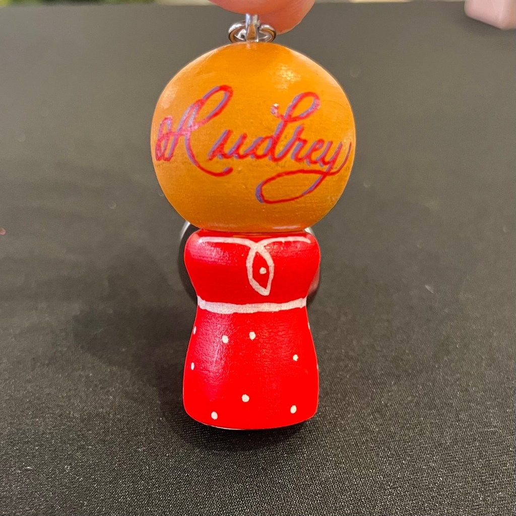 Hand painted wooden Russian doll keychain personalized with the name Audrey during an Omorovicza live event using paint pens