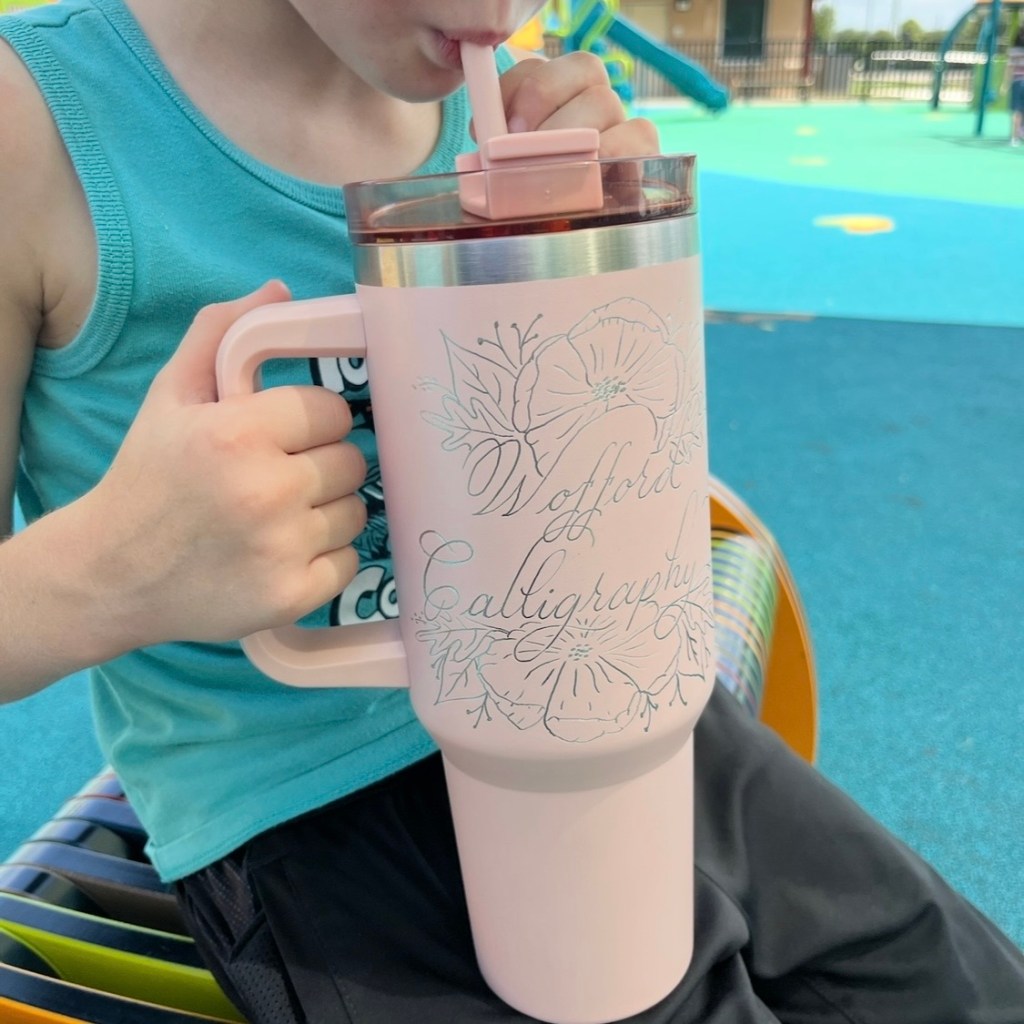 Child holding and drinking from a pink engraved business cup at a playground, showing how engraved branding is visible in everyday public spaces beyond the business owner