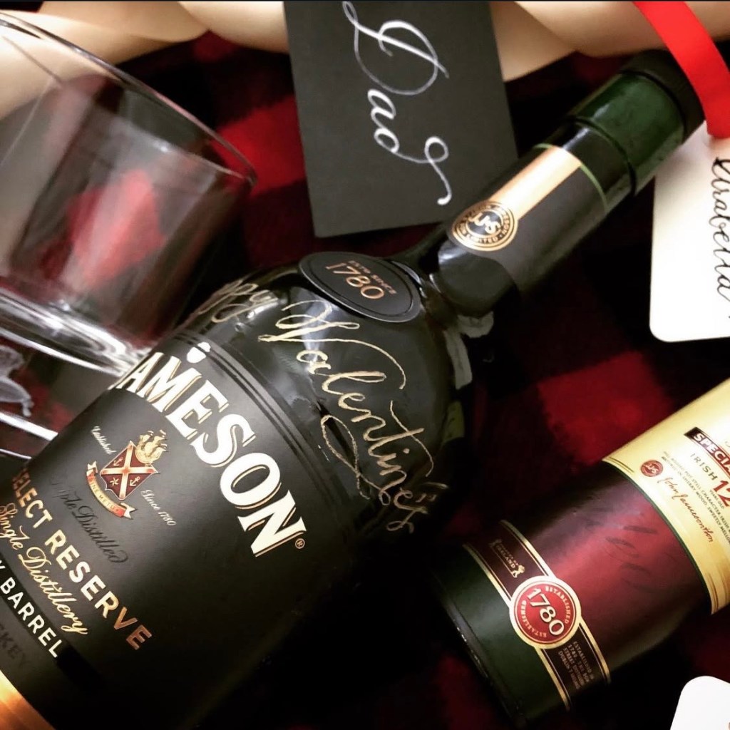 Jameson whiskey bottle engraved with “Happy Valentine’s” in calligraphy, styled with handwritten dip pen tags showing personalized Valentine’s Day gift options for him.