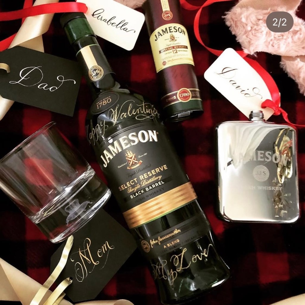 Jameson whiskey bottle engraved with “Happy Valentine’s” in gold-filled calligraphy, styled with handwritten dip pen gift tags showing Valentine’s Day gift options for him.