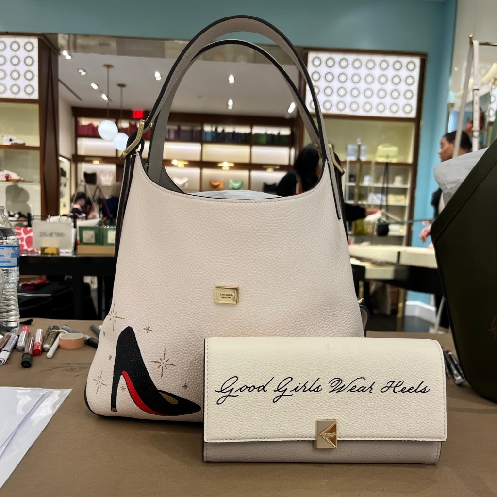 Custom hand-painted Kate Spade handbag and wallet with “Good Girls Wear Heels” calligraphy created during live luxury personalization event in Houston.