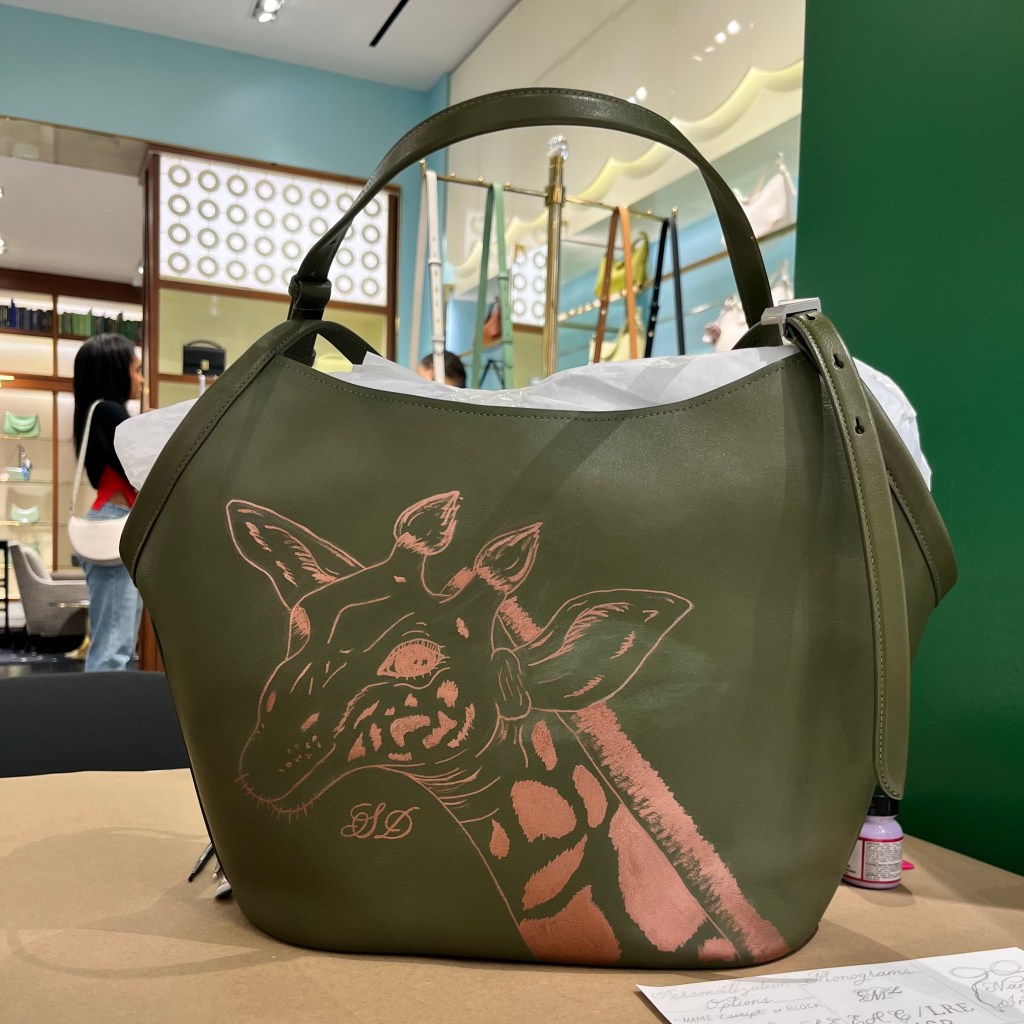 Custom hand-painted giraffe artwork on a luxury leather handbag during live personalization event in Houston.