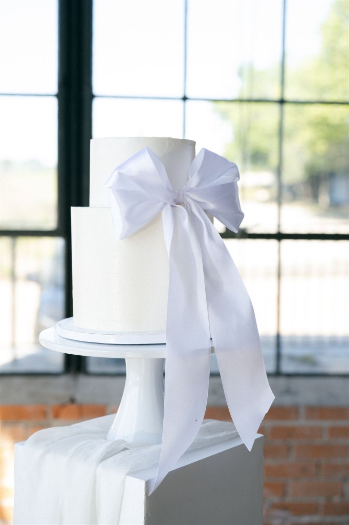 Minimal wedding cake with soft white bow, simple and elegant design emphasizing intentional wedding details and guest experience.