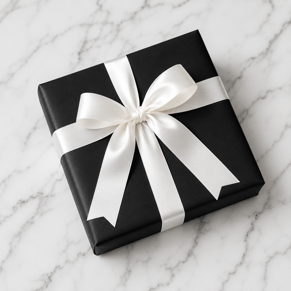 Black gift box wrapped with a wide white ribbon bow on a white marble background.