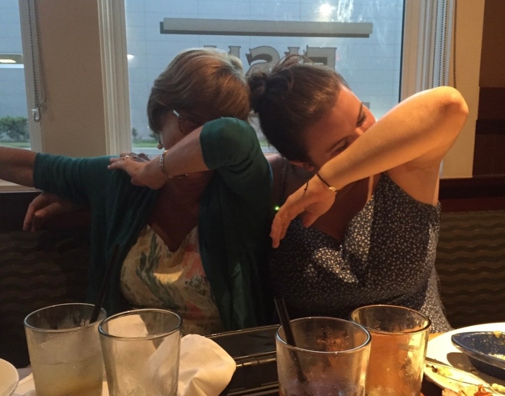 Mother and daughter laughing and doing a playful dance pose together at a family dinner.
