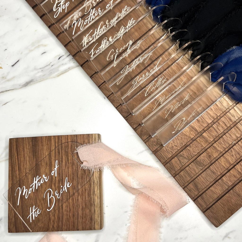 Mother of the Bride acrylic gift tag with blush ribbon beside a handcrafted walnut drying rack holding completed wedding party tags.