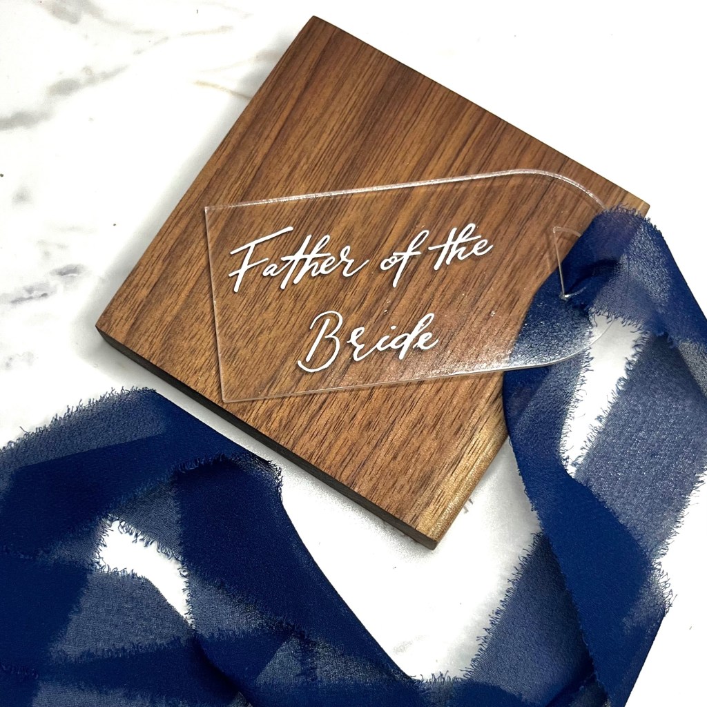 Completed acrylic wedding party gift tags featuring hand-lettered names, white calligraphy, and navy blue ribbon accents. After multiple rounds of testing, refinishing, troubleshooting, and collaboration, the final pieces were prepared for presentation to the groom's family and wedding party. This image represents the finished result of the often unseen craftsmanship that goes into handmade wedding details.