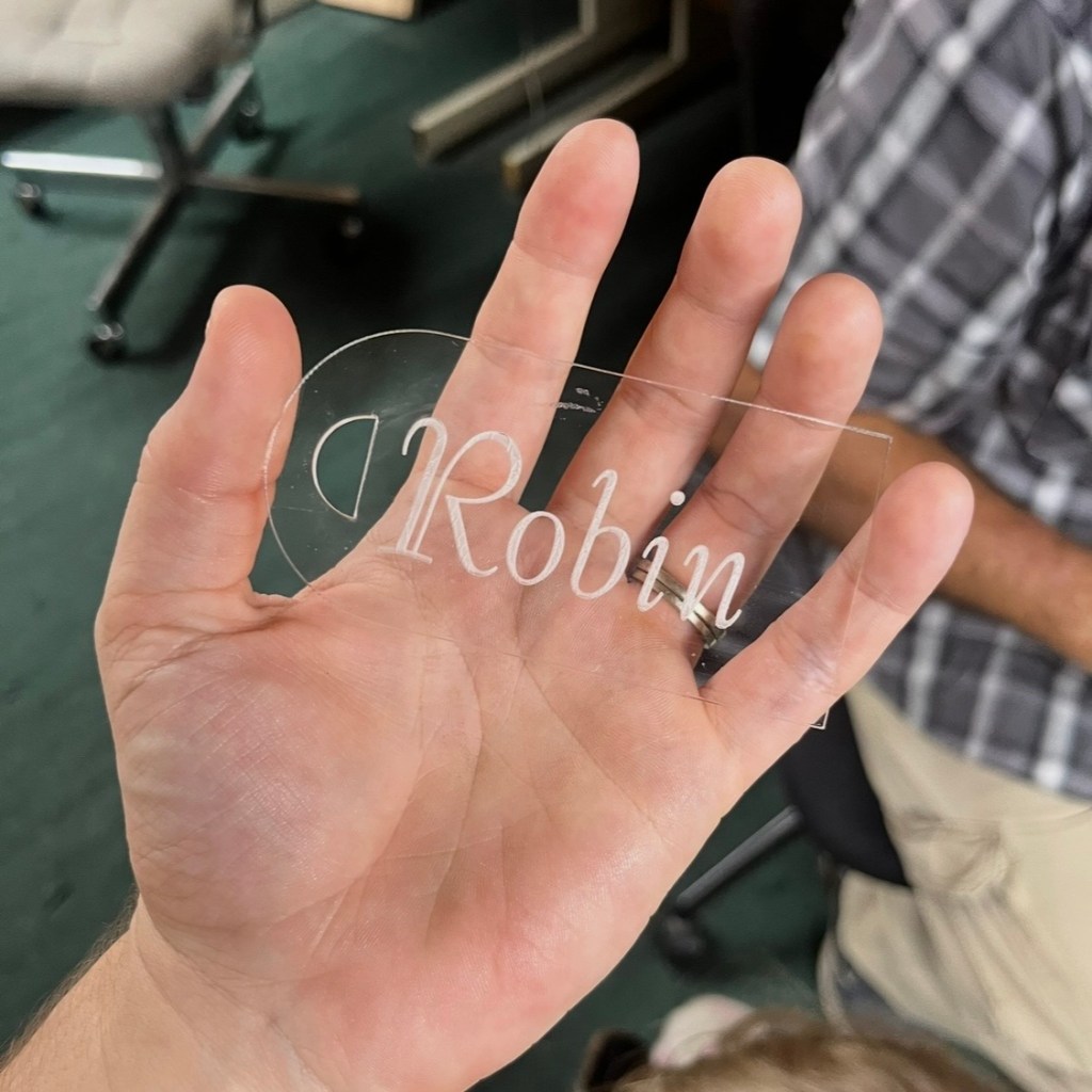 Laser-engraved acrylic wedding place card held in hand during testing at a custom fabrication workshop before final production.