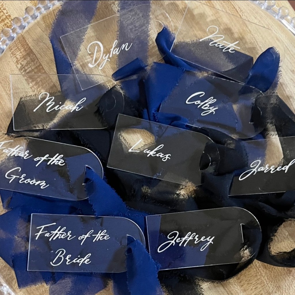 Finished acrylic wedding party gift tags with white calligraphy lettering and navy blue ribbon, prepared for presentation to groomsmen and family members.
