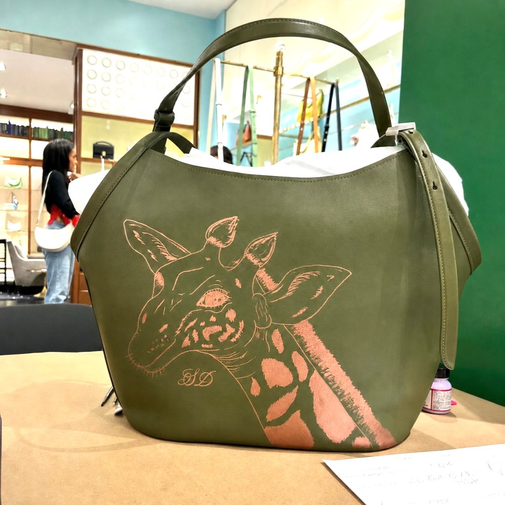 Custom hand-painted giraffe artwork on a luxury leather handbag during live personalization event in Houston.