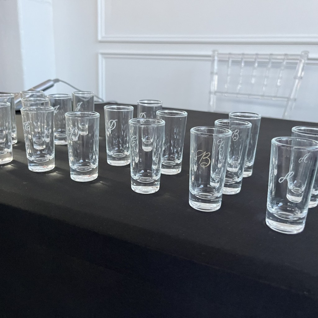 Glass shot glasses individually engraved with custom initials as an example of personalized realtor closing gifts.